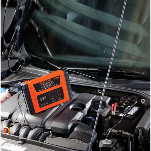 BLACKDECKER BC12 car battery charger in orange and black on engine, connected to battery terminals.