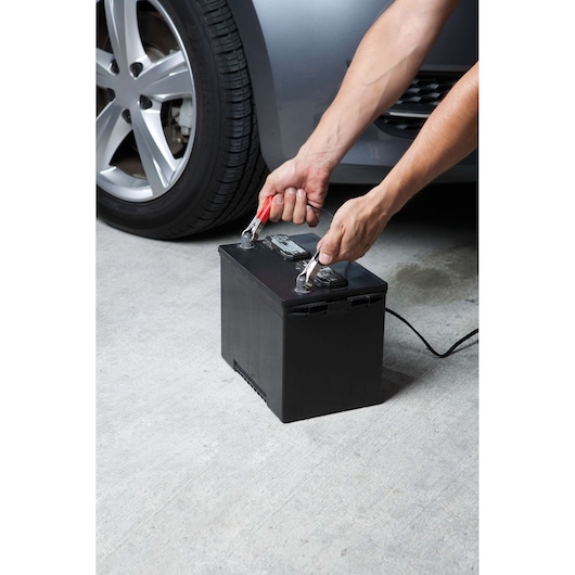 BLACKDECKER BC12 car battery charger connected to black battery by vehicle on concrete surface.