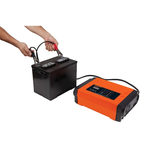 BLACKDECKER BC25 battery charger connected to a black car battery, side angle, orange casing.