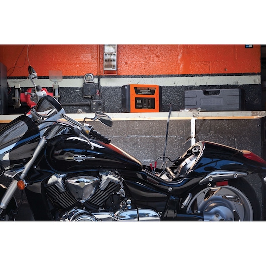 BLACKDECKER BC25 battery charger on workbench charging a motorcycle in a garage setting.