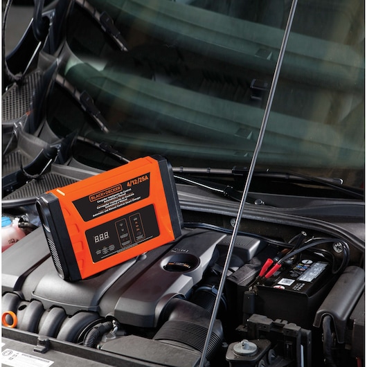 BLACKDECKER BC25 automotive battery charger placed on car engine, orange and black color, in use.