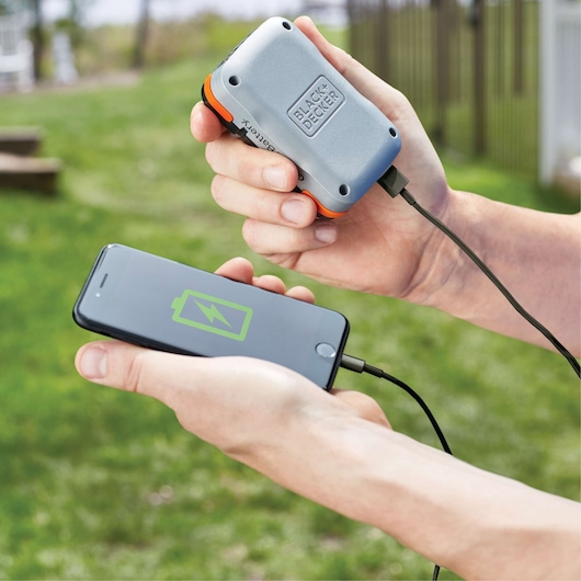 BLACK+DECKER BCB001K portable battery charging a smartphone outdoors via USB cable.