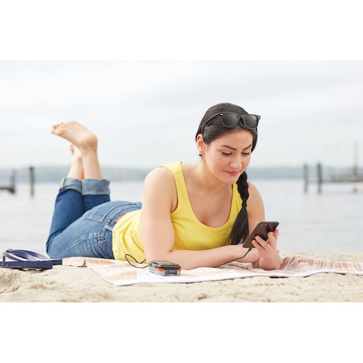 BLACKDECKER BCB001K portable charger on towel by beach, woman using smartphone nearby.