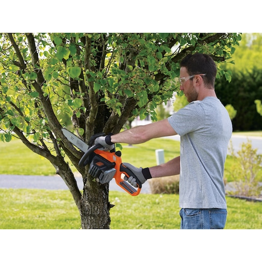 BLACKDECKER BCCS1020D1 cordless chainsaw in use cutting tree branch outdoors.