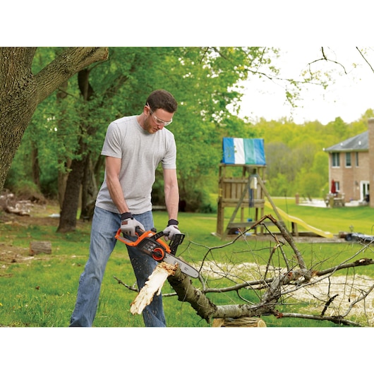 BLACKDECKER BCCS1020D1 cordless chainsaw in use, cutting a fallen tree branch in a backyard.