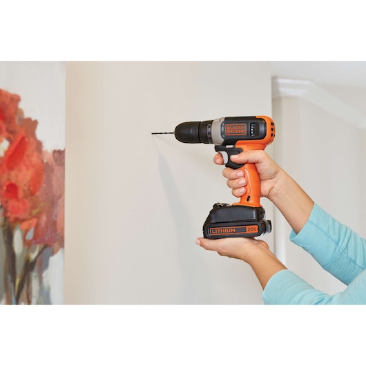 BLACK+DECKER BCD70250PK cordless drill with orange and black design in use drilling into a wall.