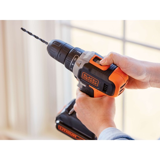 Photo of BLACK+DECKER BCD703C1 cordless drill in use, orange and black, close-up view.