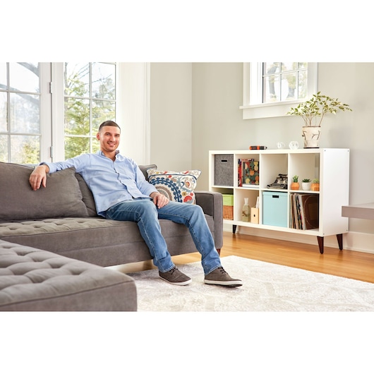 BLACKDECKER BCF601AA living room scene with a man in a blue shirt sitting on a gray sofa, storage shelf in background.