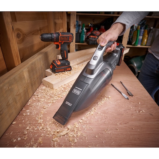 BLACKDECKER BCHV001D1E cordless handheld vacuum in use on a workbench with wood shavings, drill and bits visible.