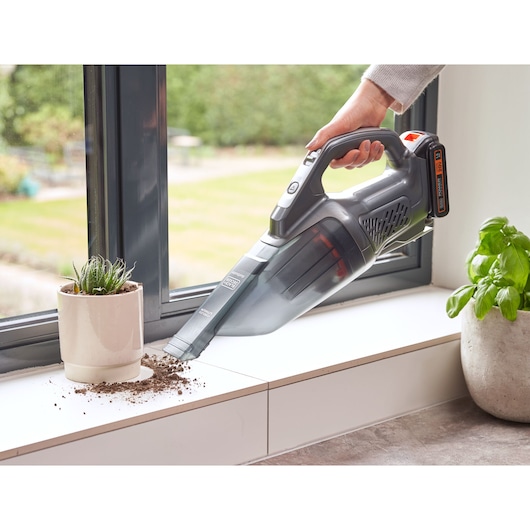 Photo of BLACKDECKER BCHV001D1E handheld vacuum cleaning soil from a windowsill near a potted plant.