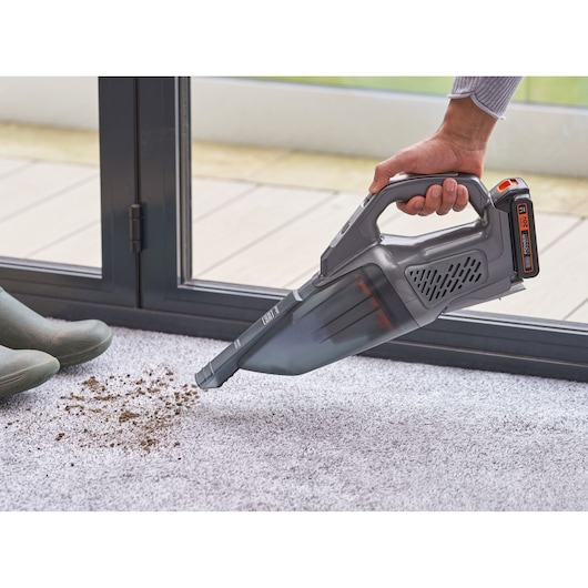 BLACKDECKER BCHV001D1E handheld vacuum cleaning dirt from carpet near boots and glass door.