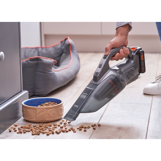 BLACKDECKER BCHV001D1E handheld vacuum cleaning pet food from floor near a pet bowl and bed, indoor scene.
