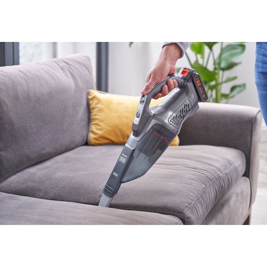 BLACKDECKER BCHV001D1E handheld vacuum cleaner used to clean a grey couch, living room setting.