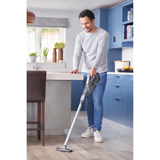 Photo of a person using a BLACKDECKER BCHV001D1E cordless stick vacuum cleaner on kitchen floor.