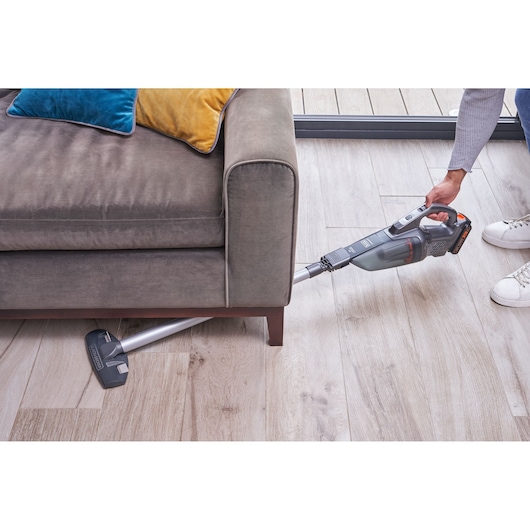 Photo of BLACKDECKER BCHV001D1E cordless stick vacuum cleaning under gray sofa on wood floor.
