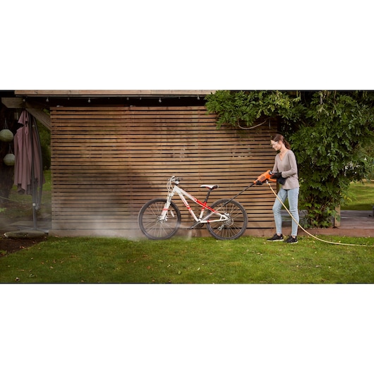 Photo of person using BLACKDECKER BCPW350E1 pressure washer to clean a bicycle outdoors on grass.