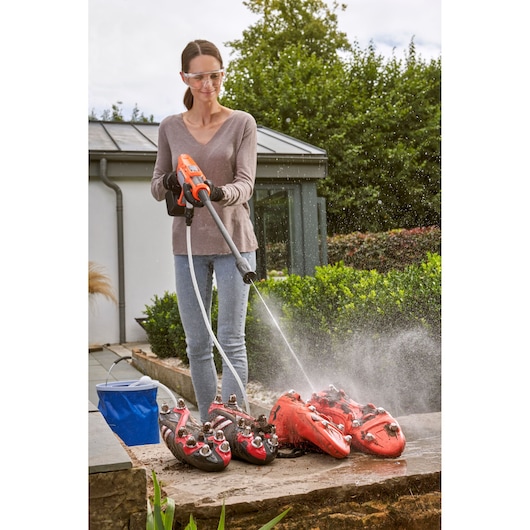 Person using BLACKDECKER BCPW350E1 pressure washer to clean dirty red sports shoes outdoors.