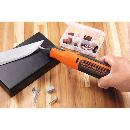 BLACKDECKER BCRT8K35 rotary tool used for sharpening a knife, accessories set visible on wooden surface.