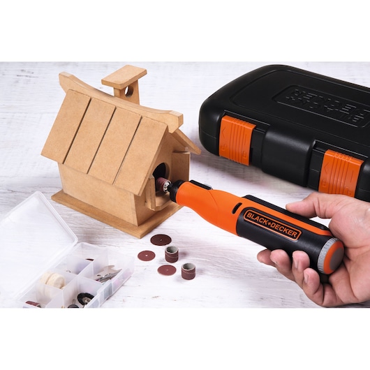 BLACKDECKER BCRT8K35 rotary tool sanding wooden birdhouse, accessory box and case on white background.
