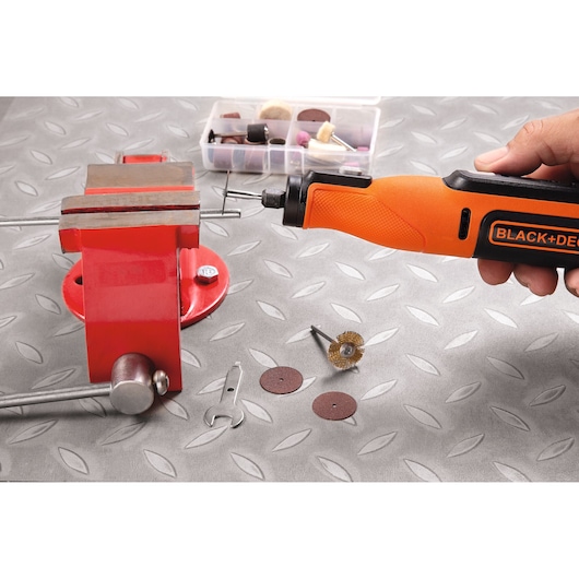 BLACKDECKER BCRT8K35 rotary tool in hand near a red vise with accessories on a metal surface.