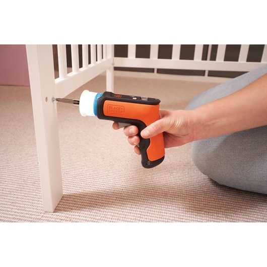 BLACKDECKER BCRTA601I orange cordless screwdriver used to assemble white furniture, side angle.