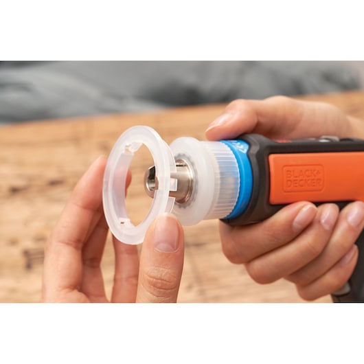Close-up of hands attaching clear plastic accessory to BLACKDECKER rotary tool BCRTA601I, orange and black handle visible.