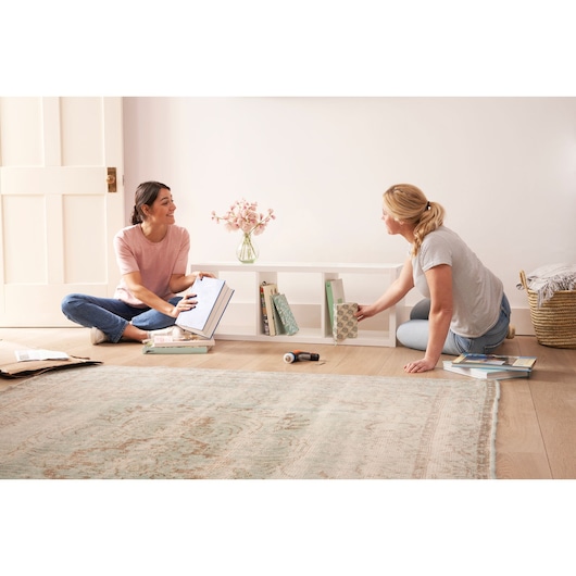 BLACKDECKER BCRTA601I cordless screwdriver on floor beside two people organizing books in a bright room.