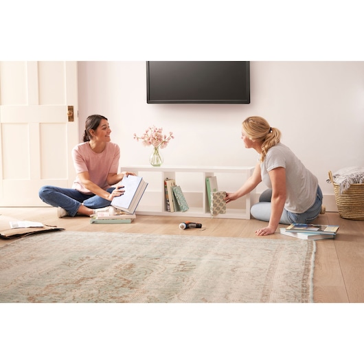 BLACKDECKER BCRTA601I cordless screwdriver on floor with two women organizing books in a living room.