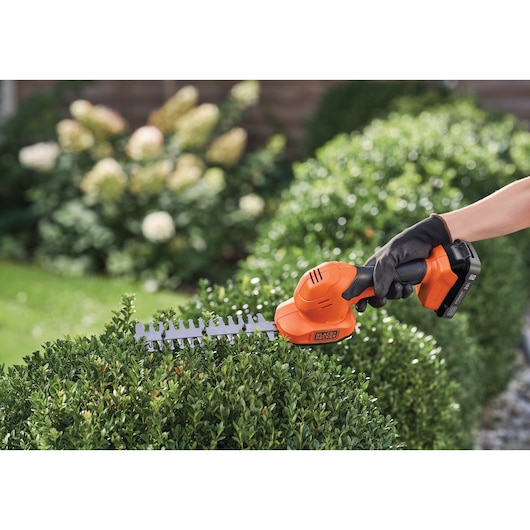 BLACK+DECKER BCSS820D1 cordless shrub shear in use trimming green bushes outdoors.