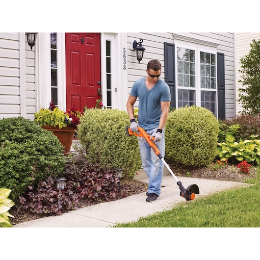 Photo of person using BLACKDECKER BCST201C1 cordless string trimmer on garden sidewalk.