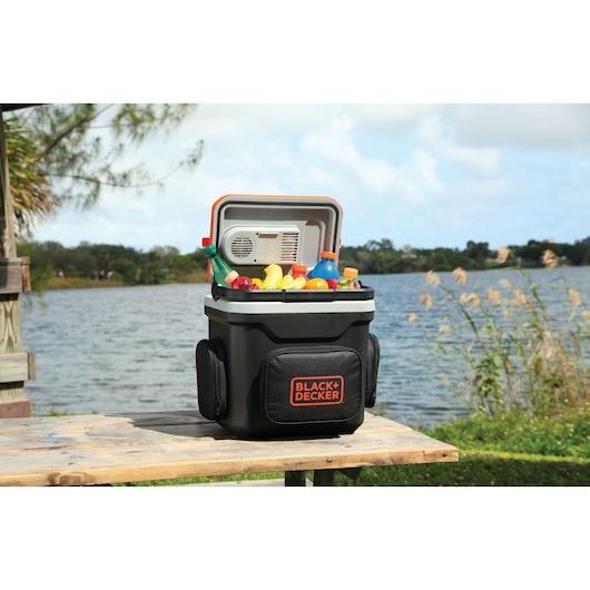 BLACKDECKER BDC24L portable cooler filled with drinks and fruit on a wooden table by a lake, outdoor setting.