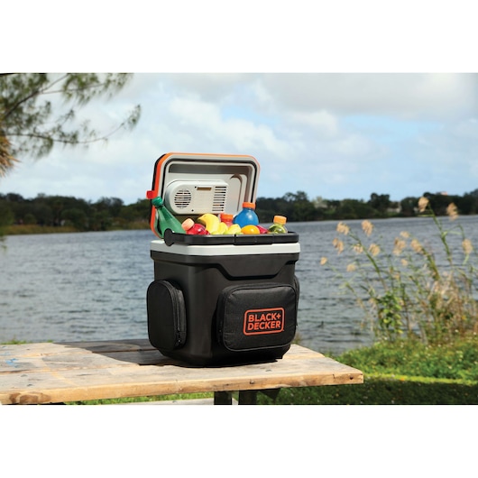 BLACKDECKER portable cooler BDC24L on a table, filled with drinks, photographed outdoors by a lake.