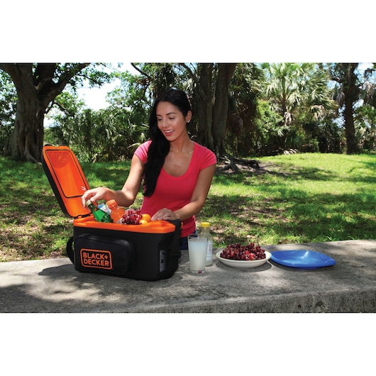 BLACK+DECKER BDC8-LA portable cooler in black and orange, open on a picnic table with drinks and fruit outdoors.