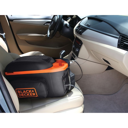 BLACK+DECKER BDC8-LA portable cooler in black and orange on car passenger seat, connected to power outlet.