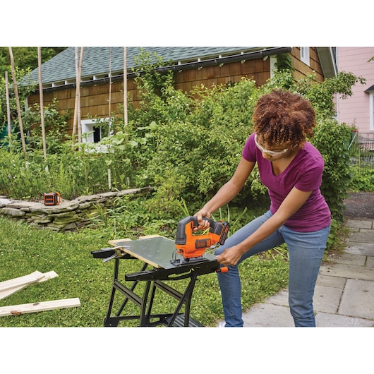 Photo of BLACKDECKER jigsaw BCK22S1S cutting wood on a workbench outdoors, used by a person wearing safety glasses.