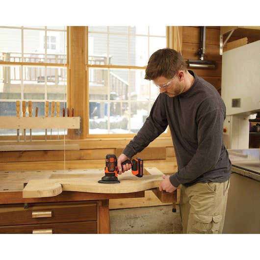 Photo of person using BLACKDECKER BDCMTS sander tool on a wooden board in a workshop.