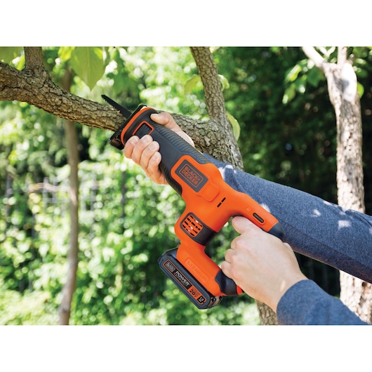 BLACKDECKER BDCR20C reciprocating saw cutting tree branch outdoors, orange and black power tool.