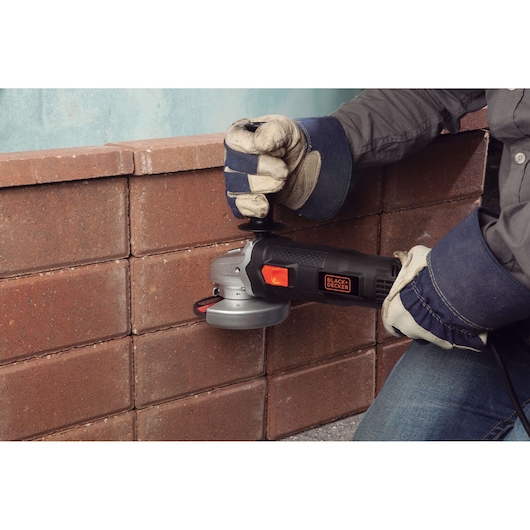 BLACKDECKER BDEG820 angle grinder being used to cut mortar between red bricks, close-up, with gloved hands.