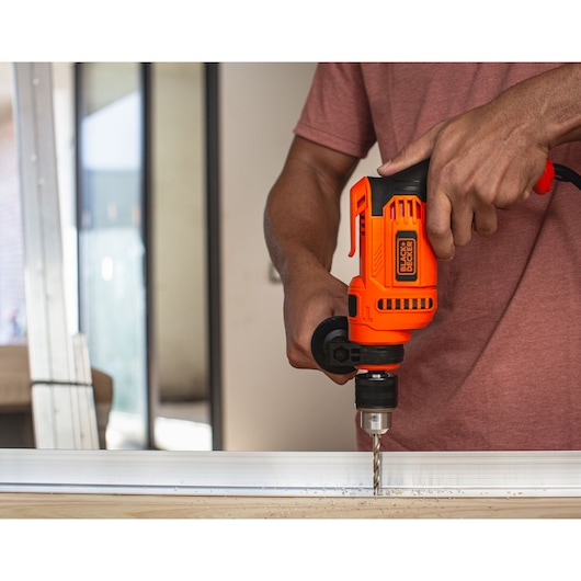 Photo of a person using a BLACK+DECKER BED713650 orange corded drill to bore into metal at close range.