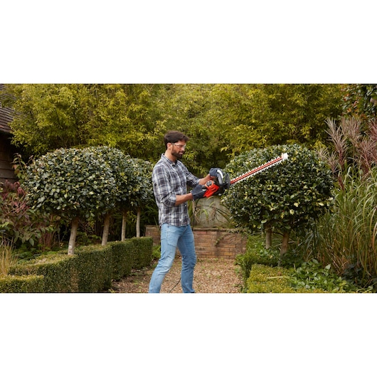 BLACKDECKER BEHTS401 hedge trimmer in use outdoors, man trimming bushes in garden.