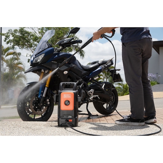 BLACKDECKER BEPW1300 pressure washer cleaning a blue motorcycle outdoors, product visible in foreground.