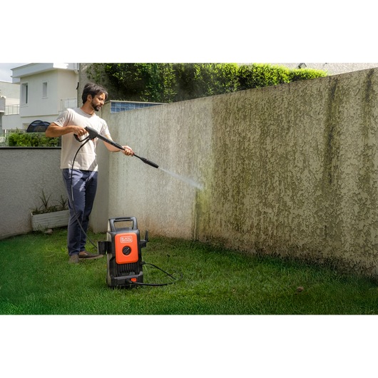 BLACK+DECKER BEPW1520 pressure washer used outdoors to clean a stained concrete wall with a high-pressure water spray.