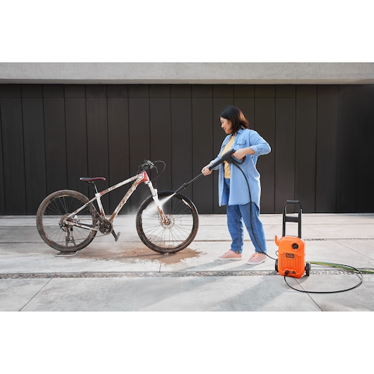 BLACKDECKER BEPW1600L pressure washer used to clean a muddy bicycle outdoors.