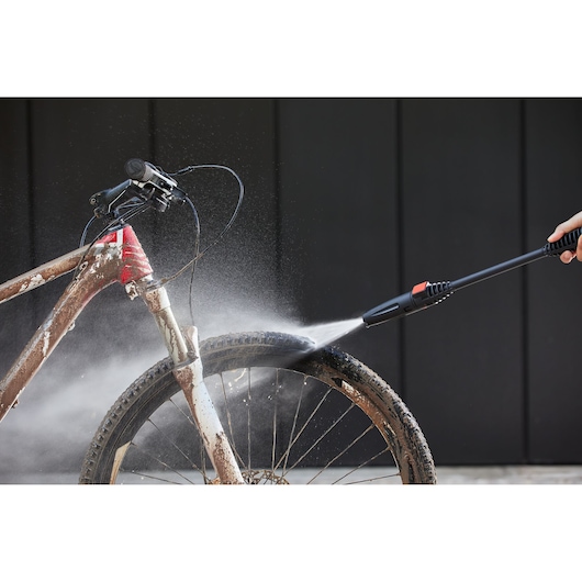 BLACKDECKER BEPW1600L pressure washer spraying water to clean muddy bicycle tire, front view.