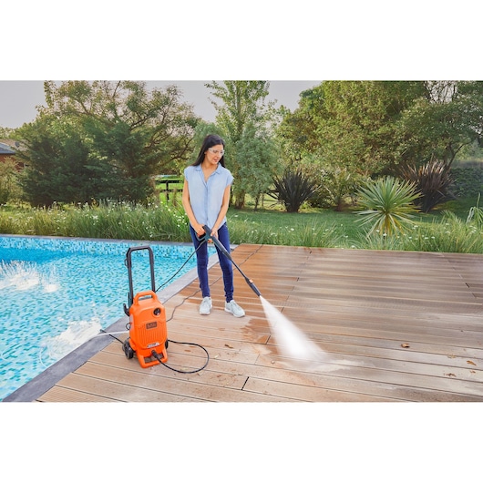 BLACKDECKER BEPW1800T pressure washer cleaning wood deck near pool outdoors.