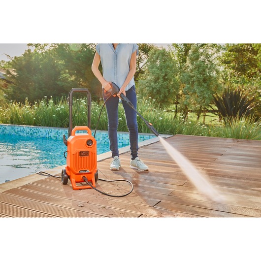 BLACKDECKER BEPW1800T pressure washer being used to clean a wooden deck near a pool.