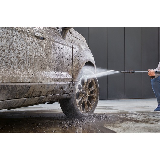 BLACKDECKER BEPW2200 pressure washer cleaning muddy car tire in action, outdoor angle.