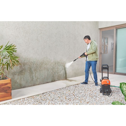 BLACKDECKER BEPW2200 pressure washer cleaning outdoor wall, person using sprayer in garden setting.