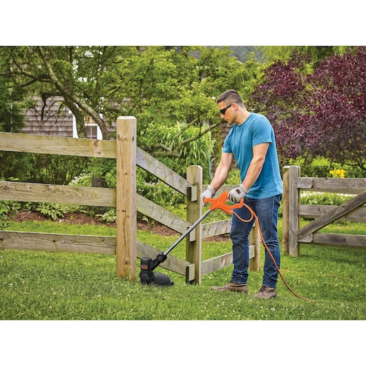 Photo of person using BLACKDECKER BEST935 electric string trimmer along wooden fence in garden.