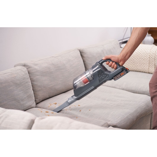 BLACKDECKER BHFEA18D1 handheld vacuum cleaner cleaning crumbs on light gray sofa upholstery.
